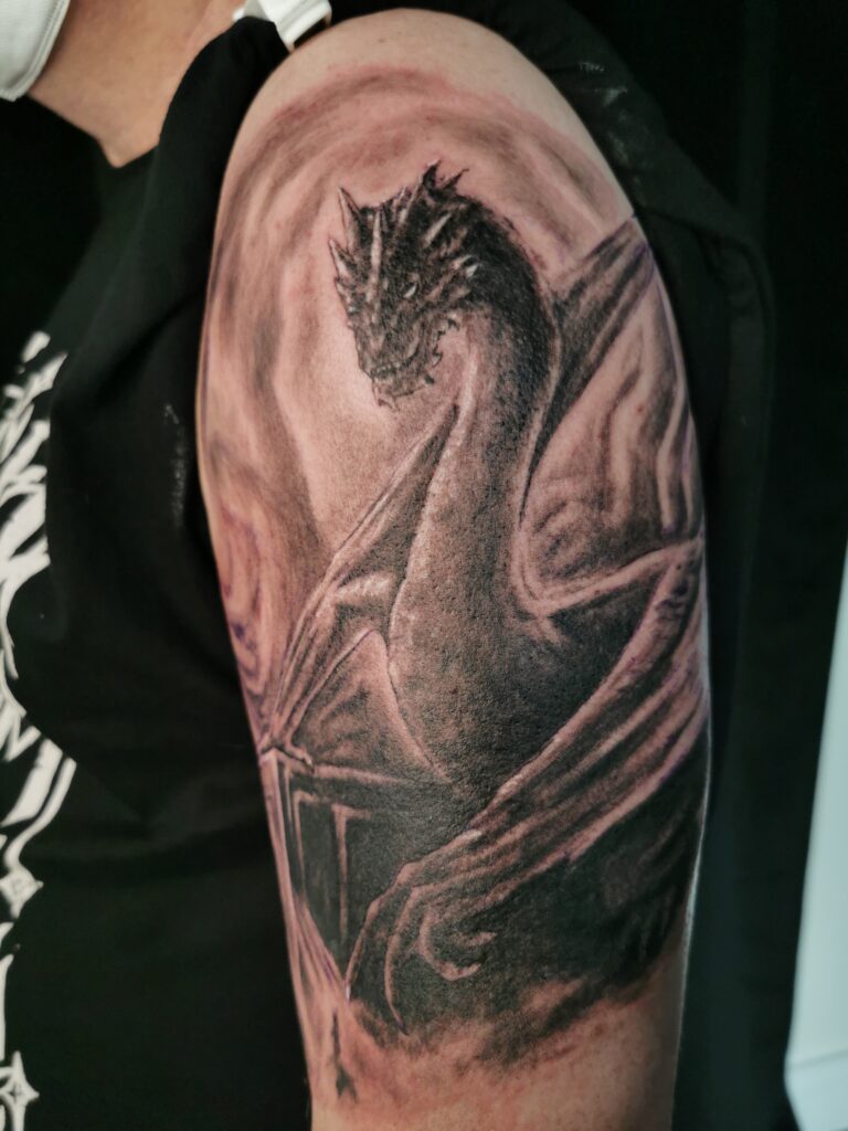 Detailliertes Drachen-Tattoo von Smaug aus Der Hobbit auf dem Oberarm, gestochen von Ozzy in Hamburg
